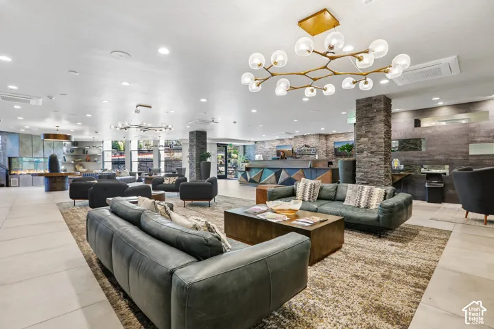 Expansive common area featuring a modern brass multi-globe chandelier, floor-to-ceiling stone pillar accents, large-format tile flooring, and a stone-clad reception desk with geometric wood paneling
