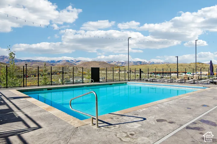 Rectangular swimming pool featuring a concrete deck, metal handrail, glass perimeter fencing, and mountain backdrop