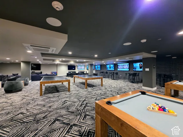 Large recreation area featuring recessed lighting, patterned carpeting, multiple wall-mounted televisions, and a drop ceiling