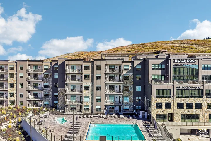 Multi-story residential complex featuring stone masonry accents, metal panel siding, private balconies, an outdoor swimming pool, and an in-ground spa