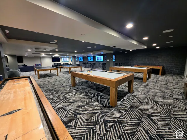 Spacious recreation area featuring recessed lighting, a dark-toned drop ceiling, textured accent walls, and patterned carpeting