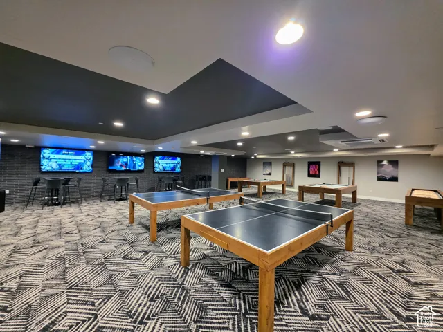 Large interior space featuring a recessed tray ceiling, patterned carpeted flooring, and a floor-to-ceiling textured brick accent wall