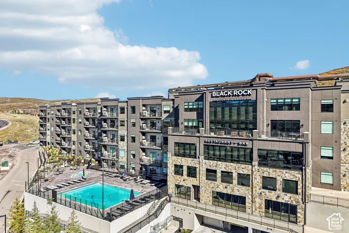 Multi-story residential complex featuring stone masonry facade, private balconies, an outdoor swimming pool, and dedicated parking structure