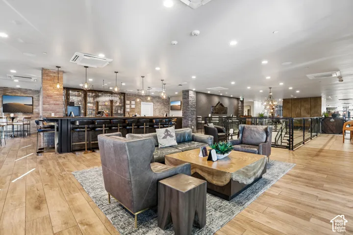Built-in bar with stone-accented columns, wood-finish flooring, recessed ceiling lighting, and glass-railing staircase