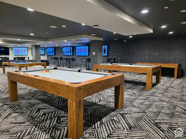 Large open room featuring recessed lighting, dark brick accent wall, patterned wall-to-wall carpeting, and multiple integrated wall-mounted screens