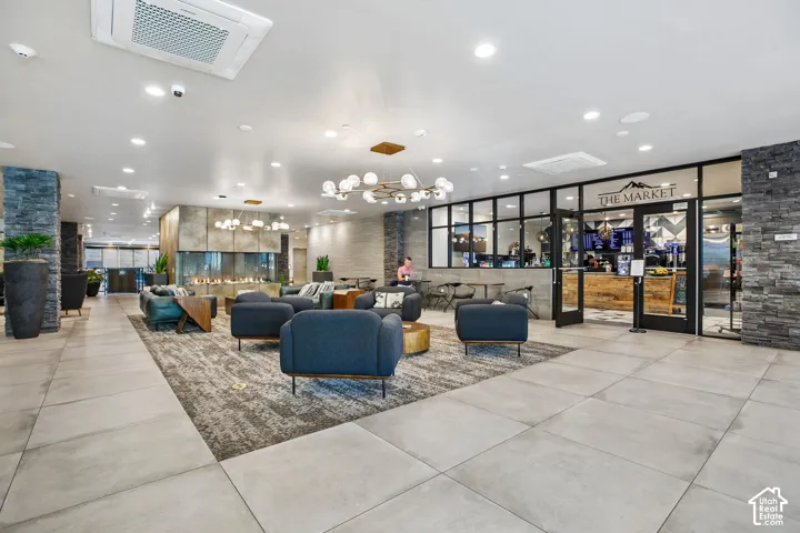 Common area featuring large-format tile flooring, stacked stone columns, a dual-sided linear fireplace with metallic paneling, and a partitioned space with a glass-paneled entry