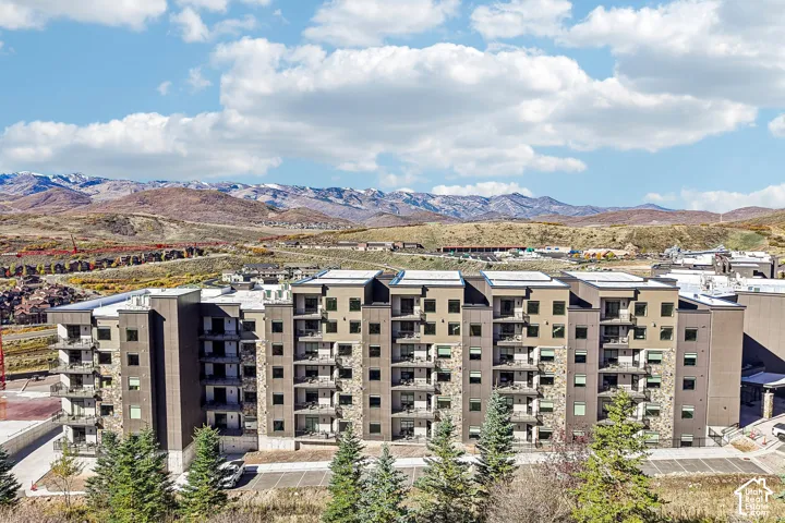 Multi-story residential building featuring mixed-material exterior cladding, stone veneer accents, private balconies, and a mountain range backdrop