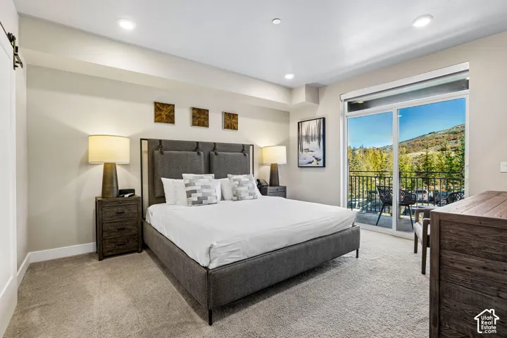 Neutral-toned carpeted bedroom featuring recessed lighting, a sliding glass door, and a private balcony with metal railing and mountainous terrain backdrop