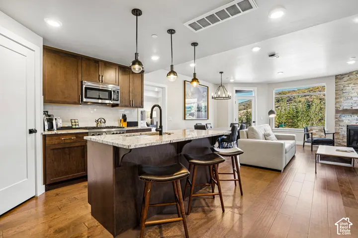 Kitchen featuring stained wood cabinetry, stone-surface island countertop, recessed ceiling lighting, three pendant lights, and wood-finish flooring