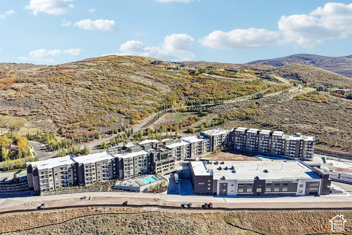 Aerial perspective of a multi-story residential complex featuring stone and siding facades, an outdoor swimming pool, and hillside terrain