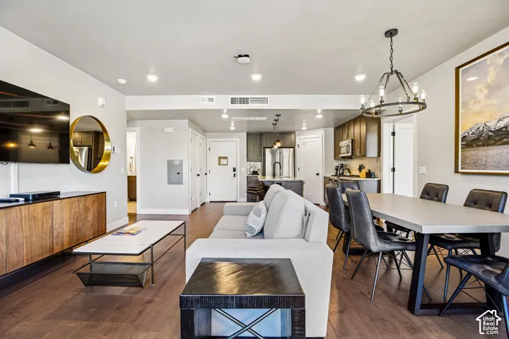 Open-concept living space featuring wood-finish flooring, recessed lighting, a modern iron chandelier, dark-toned kitchen cabinetry, and an island with stainless steel appliances