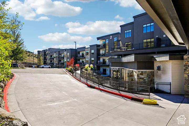 Multi-story complex featuring dark-toned metal cladding, stone veneer accents, integrated balconies with metal railings, and a concrete driveway