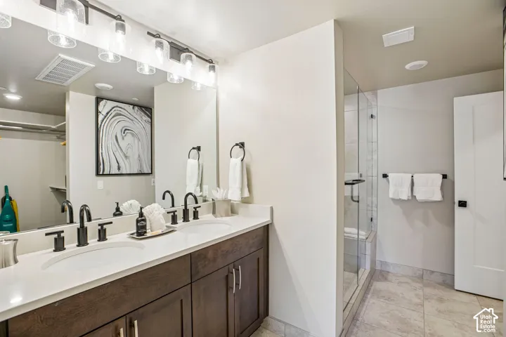 Dual-sink vanity with a quartz countertop, dark wood-finish cabinetry, matte black hardware, and a glass-enclosed shower with tile flooring