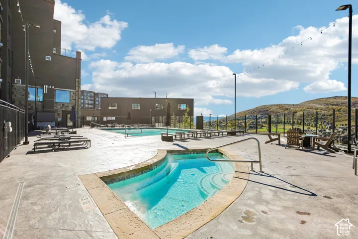 Outdoor terrace featuring a concrete pool deck, recessed spa, swimming pool, string lighting, and mountain backdrop