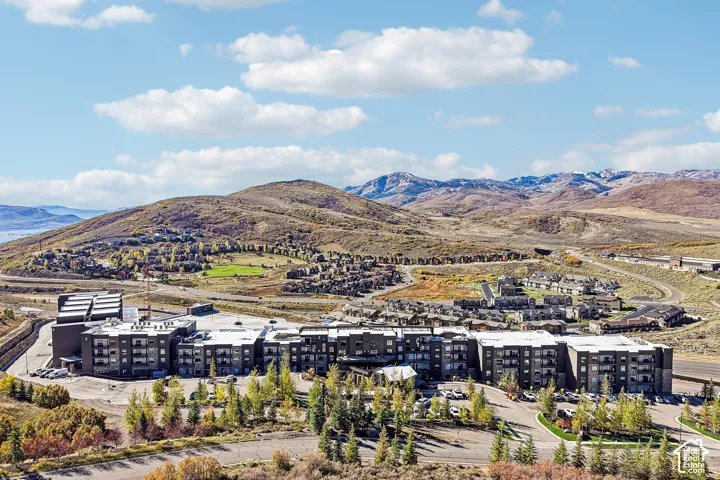 Multi-story residential complex featuring dark-toned masonry and metal siding, private balconies, paved surface parking, and extensive mountain backdrops