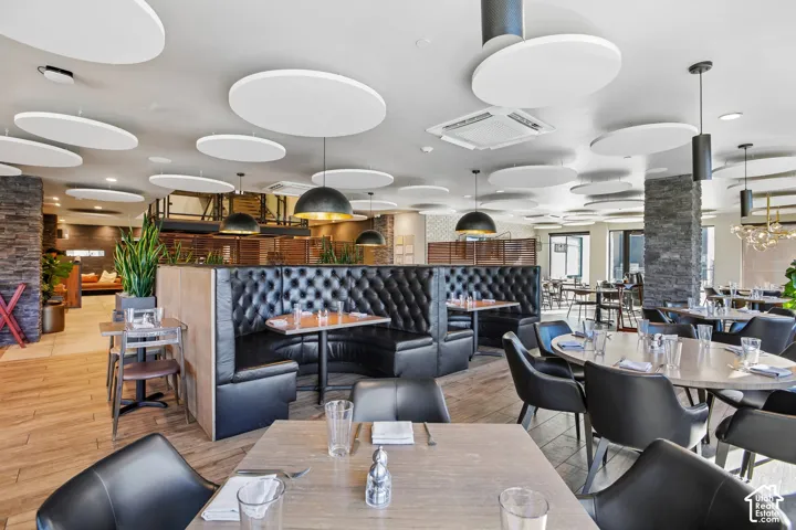 Open-concept interior featuring wood-finish flooring, stone-clad pillars, tufted leather booth seating, and ceiling-mounted acoustic discs