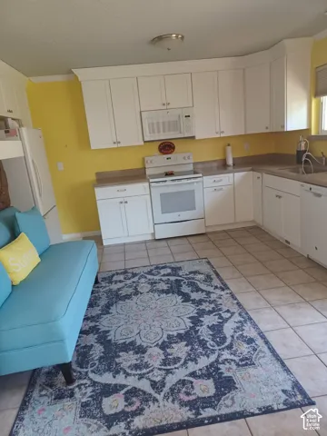 Kitchen featuring white Shaker-style cabinetry, solid-surface countertops, tile flooring, and integrated white appliances