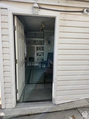 Exterior entry featuring light-colored horizontal siding, a traditional paneled door, and a mounted outdoor light fixture, opening into an interior space with built-in wall shelving and tile flooring