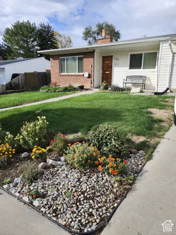 Single-story exterior featuring a brick and horizontal siding facade, chimney, and landscaped front yard with decorative stone ground cover