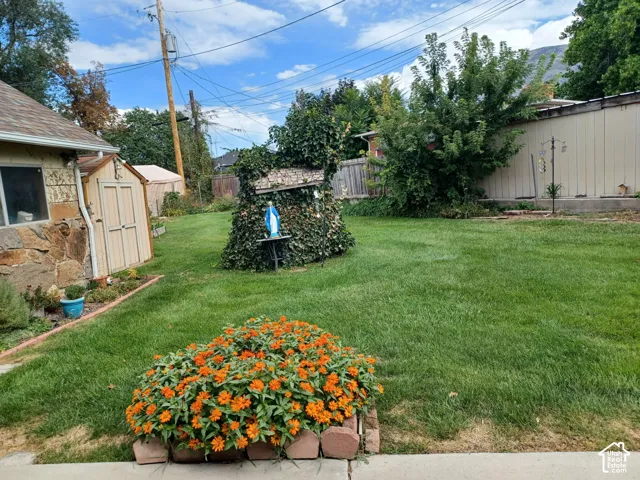 Backyard featuring a manicured lawn, a garden bed with stone edging, and a utility shed with stone veneer exterior