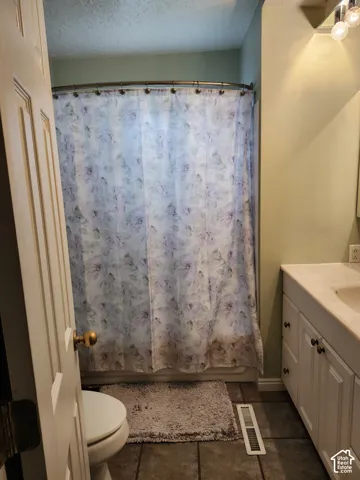 Bathroom featuring a vanity with integrated sink, stone-finish countertop, white cabinetry with dark hardware, a bathtub with a curved curtain rod, and tile flooring