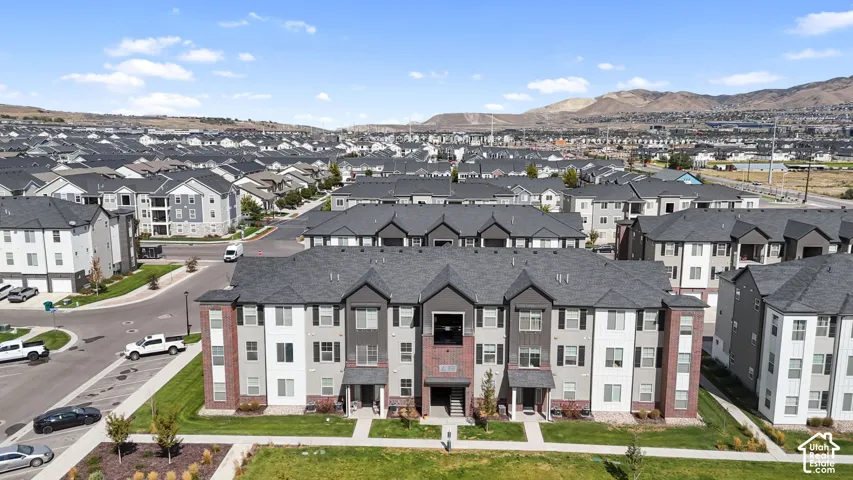 Aerial perspective of multi-story residential building featuring a mixed masonry and siding exterior, asphalt shingle roofing, paved surface parking, and a backdrop of mountain scenery