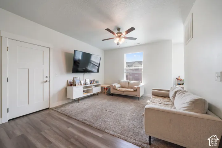 Living area featuring wood-finish flooring, a multi-panel door with craftsman-style trim, a single-hung window, and a ceiling-mounted fan with integrated lighting