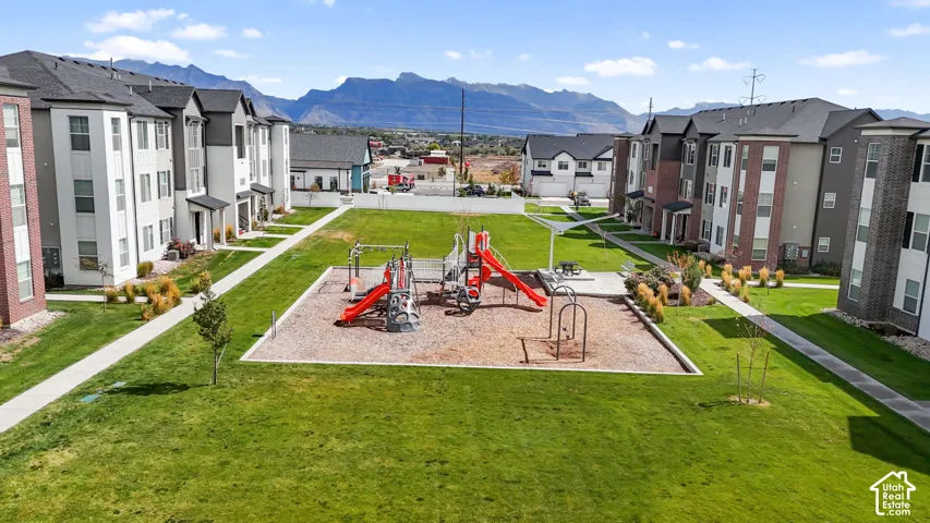 Multi-story residential complex featuring a central courtyard, integrated playground equipment, paved pedestrian paths, manicured lawns, and a mountain range backdrop