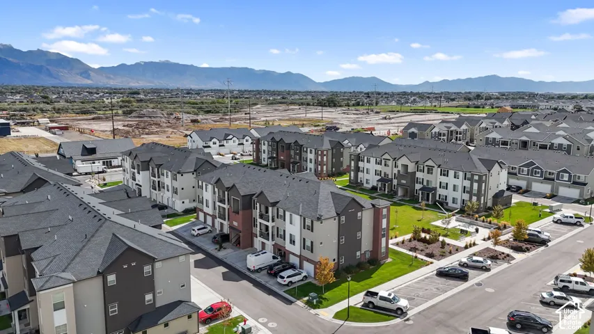 Multi-story residential buildings featuring multi-tonal siding and asphalt shingle roofing, situated within a planned community with manicured green spaces and prominent mountain backdrop
