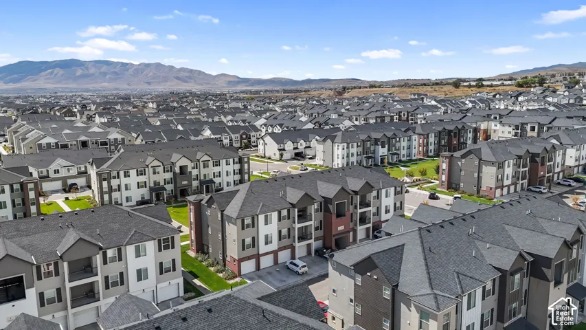 Multi-story residential complex featuring neutral-toned siding, brick accents, shingled roofing, and a mountain range backdrop