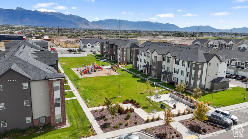 Multi-unit residential complex featuring a central playground, landscaped lawn, paved walkways, and mountain scenery