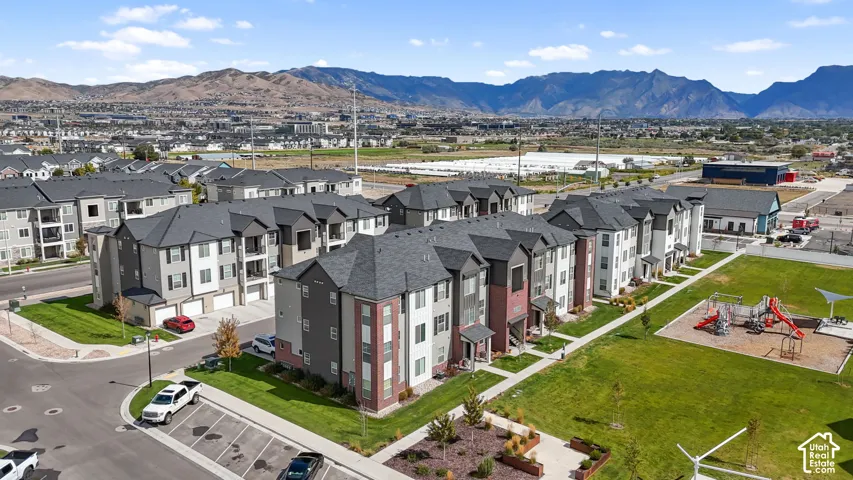 Multi-story residential buildings featuring brick and neutral-toned exteriors, asphalt shingle roofing, integrated garage parking, a landscaped communal lawn, and an on-site playground area
