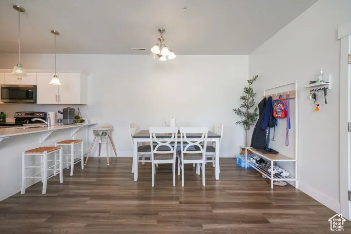 Open-concept area featuring wood-finish flooring, white cabinetry, a kitchen island with pendant lighting, and a multi-light chandelier
