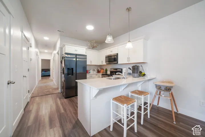 Kitchen featuring white shaker-style cabinetry, wood-finish flooring, a quartz-topped peninsula, and two glass pendant lights