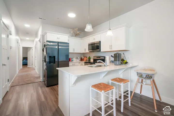 Kitchen featuring white shaker-style cabinetry, quartz countertops, a stainless steel dual-basin sink, recessed lighting, and a breakfast bar