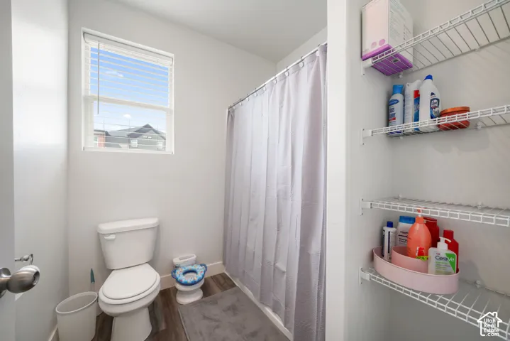 Bathroom featuring wood-finish flooring, a window with horizontal blinds, and built-in wire shelving