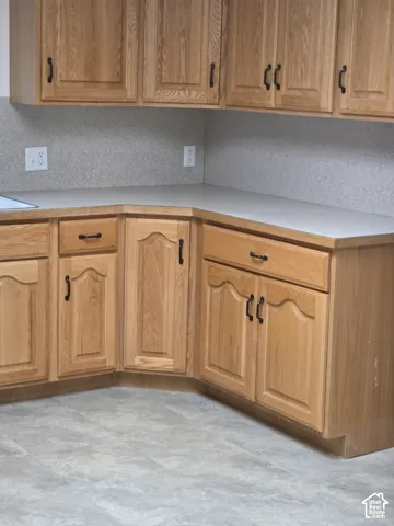 Wood-finish cabinetry featuring raised-panel doors and matte black hardware, paired with solid-surface countertops, a neutral-toned backsplash, and resilient sheet flooring