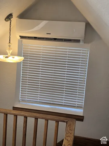 Wall-mounted ductless HVAC unit, window with horizontal blinds, and a suspended glass pendant light fixture above a wooden balustrade