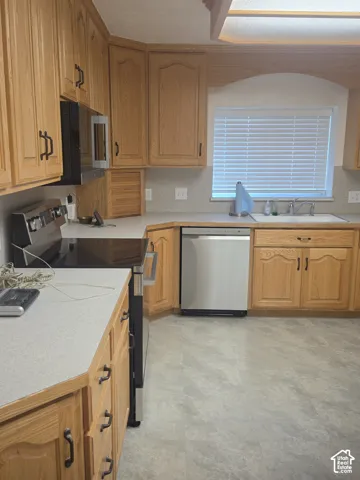 Kitchen featuring oak cabinetry, stainless steel appliances, neutral countertops, a built-in microwave, and an undermount sink