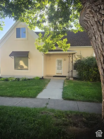 Stucco exterior featuring a steep gabled roofline, covered front entryway, metal window awning, and manicured landscaping