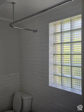 Bathroom featuring white rectangular subway tile wall cladding, a glass block window, and a polished chrome shower curtain rod