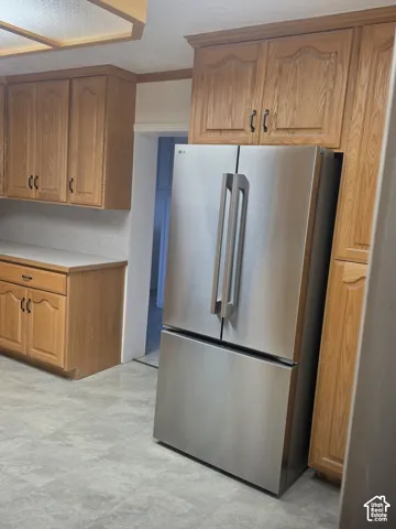 Kitchen featuring natural wood cabinetry, stainless steel French-door refrigerator, and solid-surface countertops