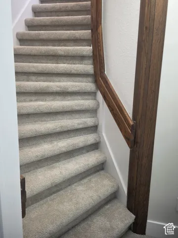 Staircase featuring wall-to-wall carpeting and a stained-wood handrail with square-profile wooden balusters