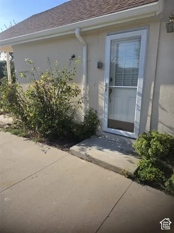 Exterior entrance featuring a concrete porch, glass-panel storm door, stucco siding, and wall-mounted exterior lighting