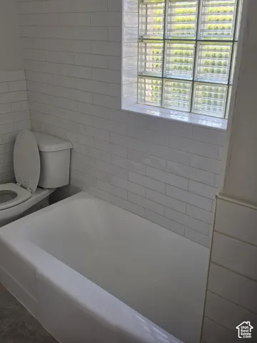 Bathtub enclosure featuring white horizontal wall tile, glass block window, and white porcelain toilet
