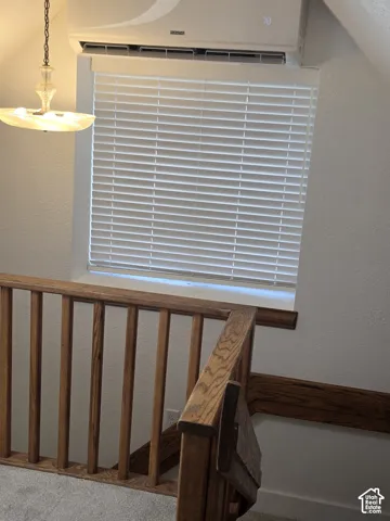 Wall-mounted ductless climate control unit, wood railing with matching wall trim, window with integrated horizontal blinds, and a multi-tiered glass pendant fixture