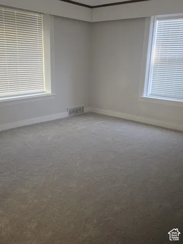 Neutral-toned wall paint, plush carpeting, horizontal blinds, and corner windows with decorative crown molding