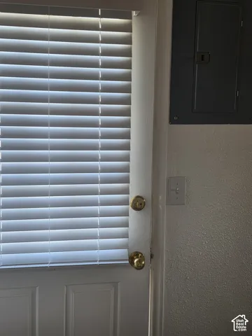 Solid white entry door featuring horizontal slatted blinds, brass-finish hardware, and a wall-mounted electrical service panel