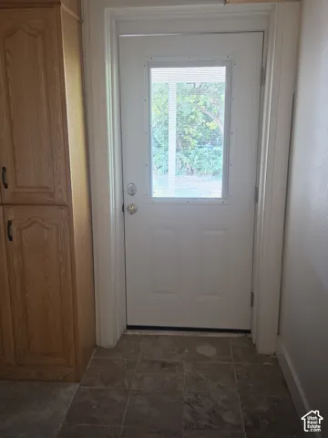 White exterior door with glass pane, light-toned wood-finish cabinetry, and stone-tile flooring