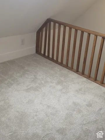 Vaulted ceiling with angled walls and a natural wood-finish balustrade, featuring neutral carpeting